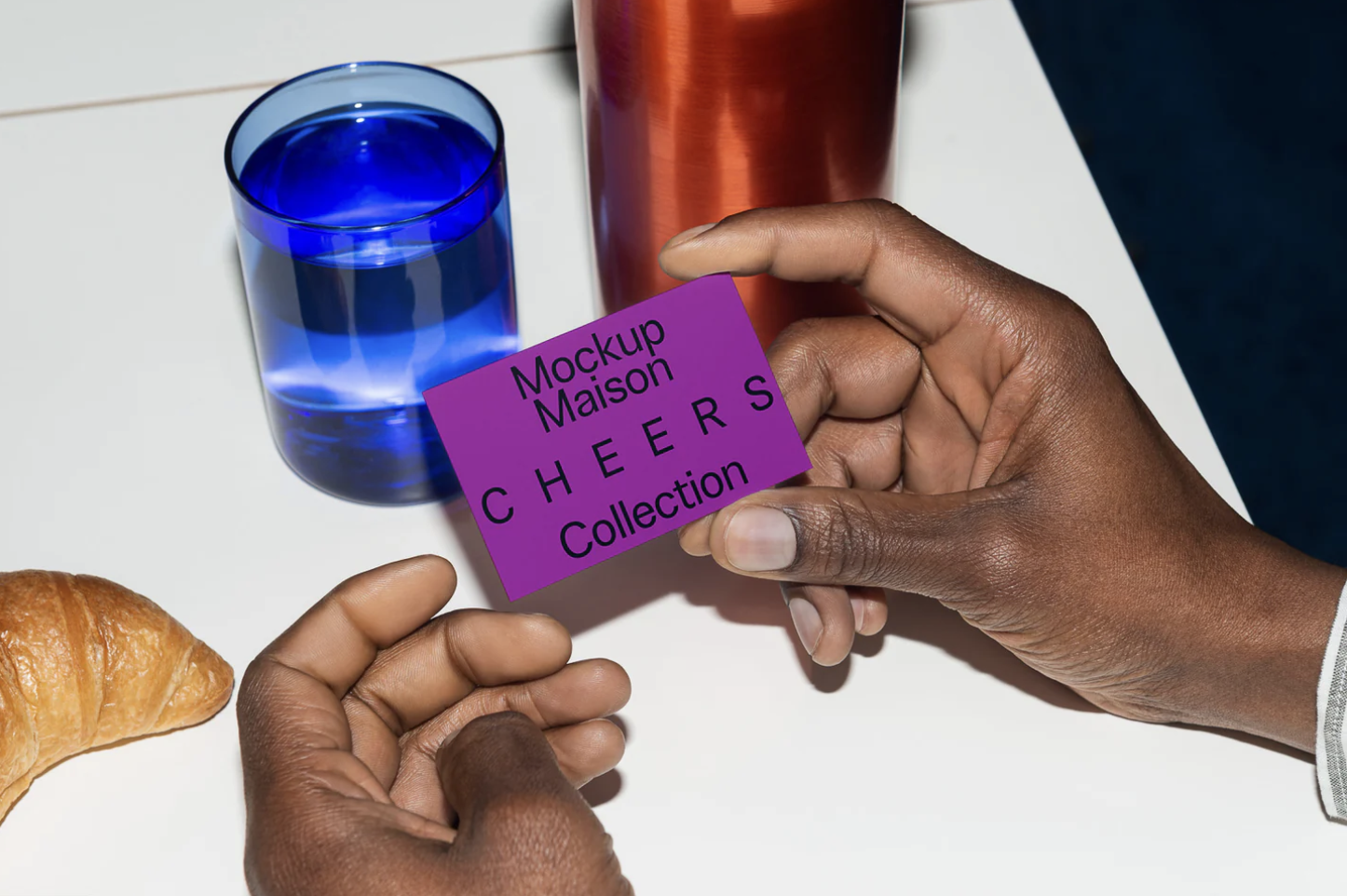 Hands holding a purple EU business card mockup near a croissant and blue glass on a white surface.