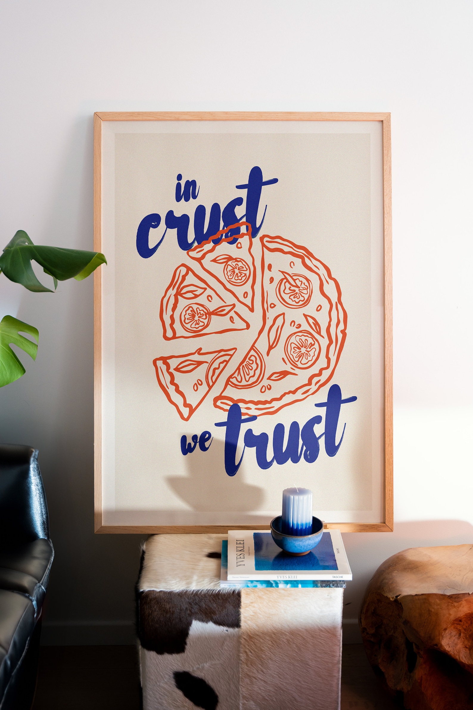 Free poster mockup of a wood-framed pizza poster with playful typography, set in a cozy modern space with arty decor elements.