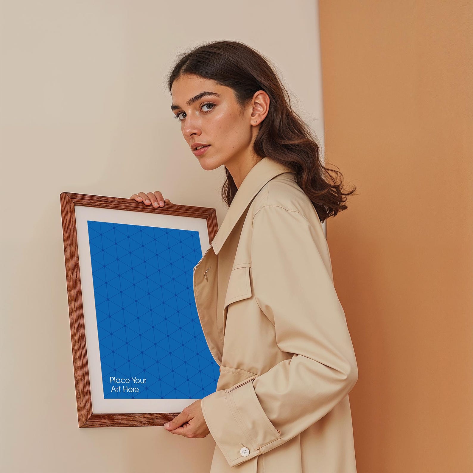 A woman in a trench coat holds a wooden-framed artwork, perfect for free poster mockups with soft lighting and natural tones.