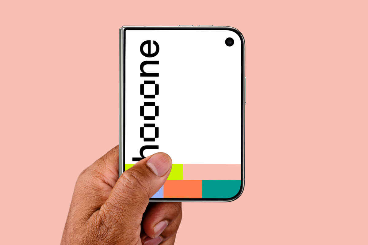 Tight crop of a closed iPhone Duo held from the lower-left corner on blush pink
