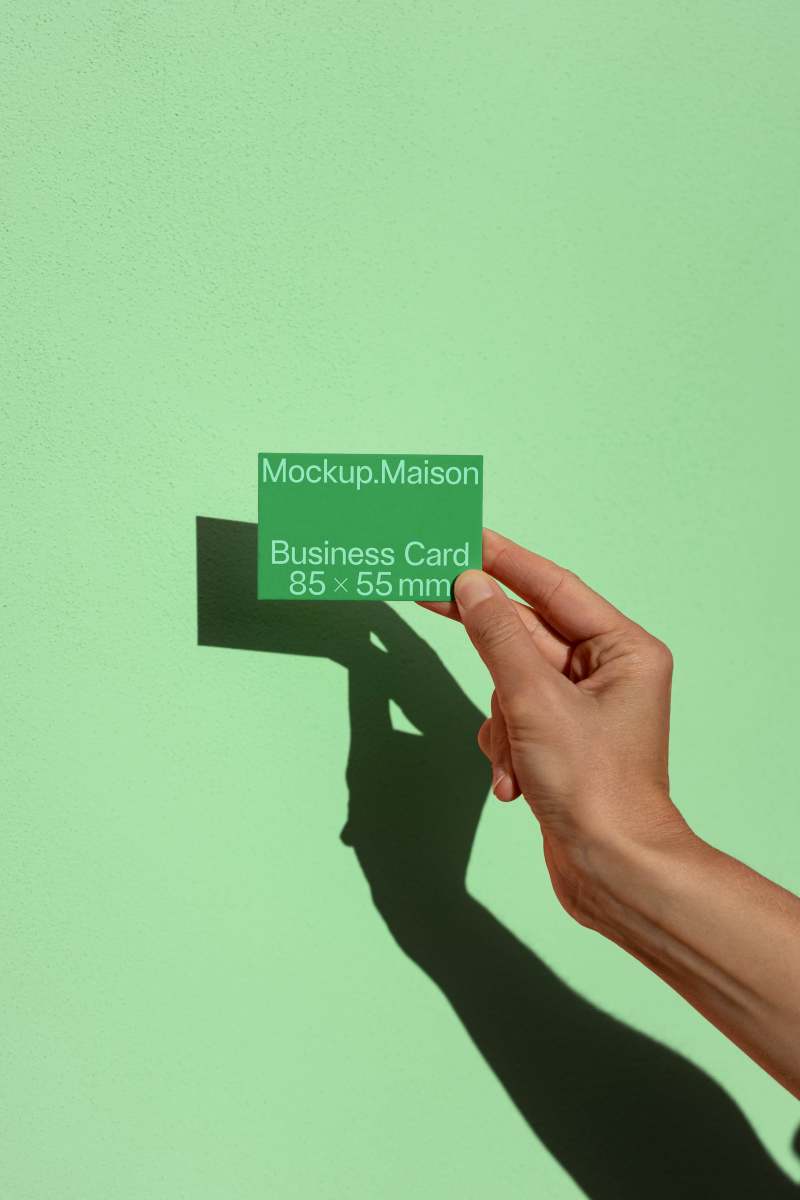 Hand holding an EU business card mockup against a green background, showcasing the minimalist design and dimensions.