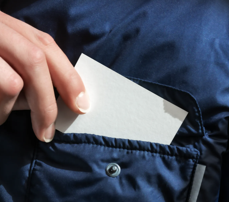 Hand placing a blank card into a dark jacket pocket, ideal for showcasing the best EU business card mockups.